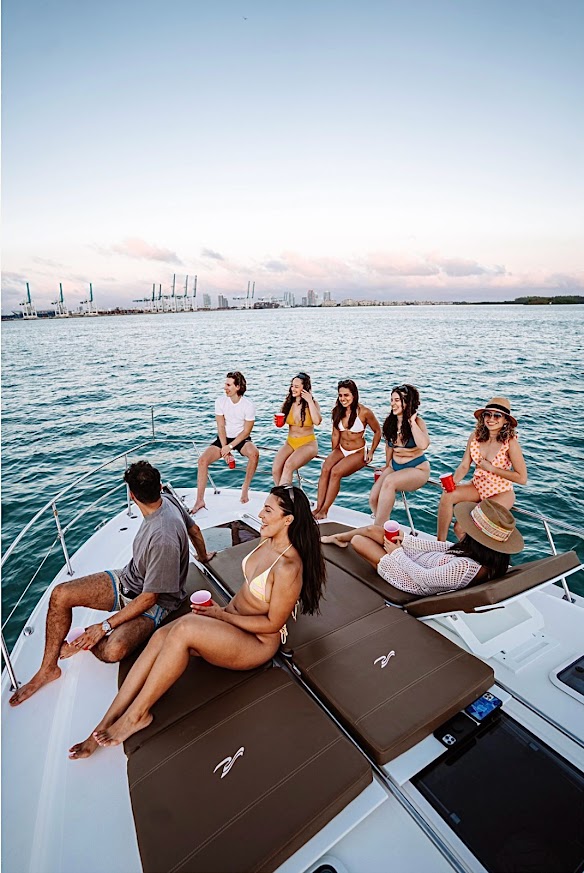 Group of guests relaxing on the bow of the 40 Sea Ray yacht at sunset in Miami Bay with the city skyline in the background