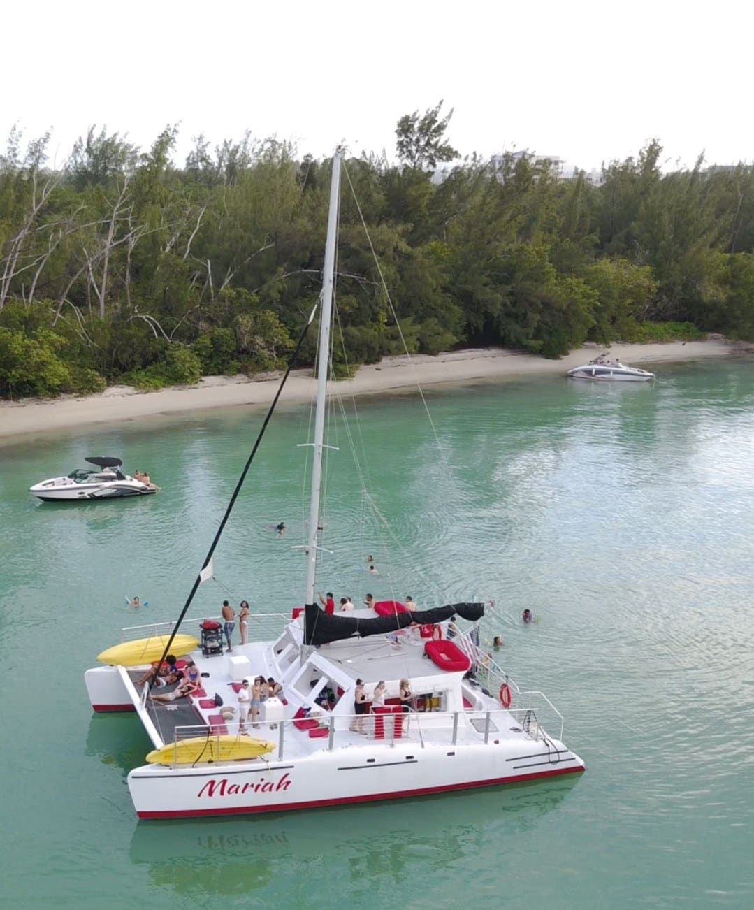 Overhead view of the Mariah sailing catamaran with guests on red cushions and swimmers in turquoise water