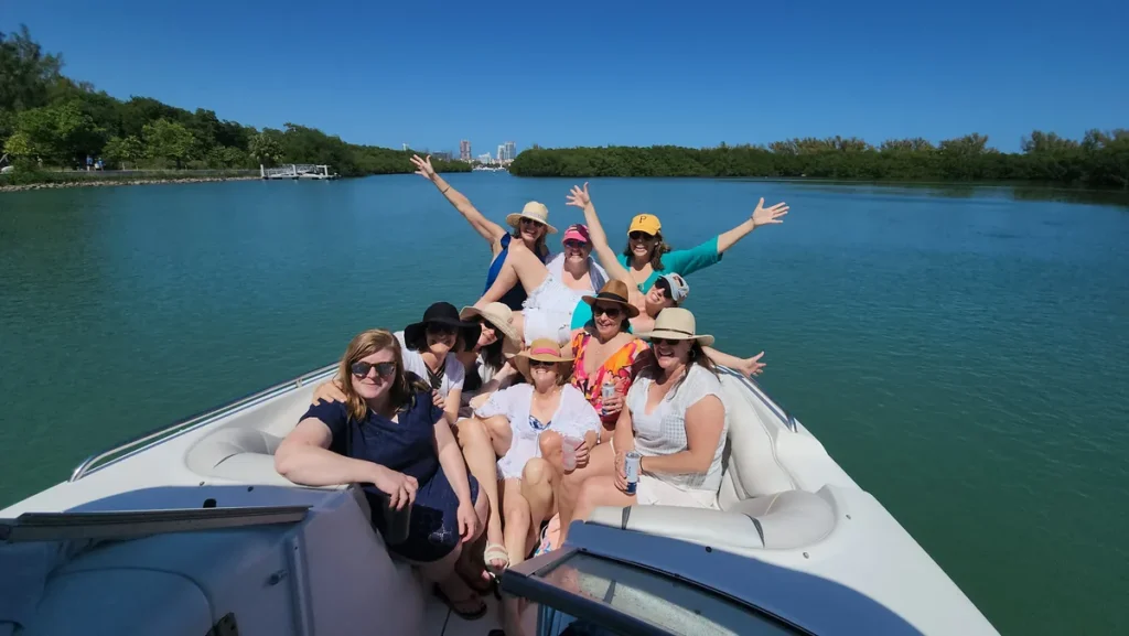 Smiling group of women of all ages waving from the bow of a boat on a sunny Miami bay outing