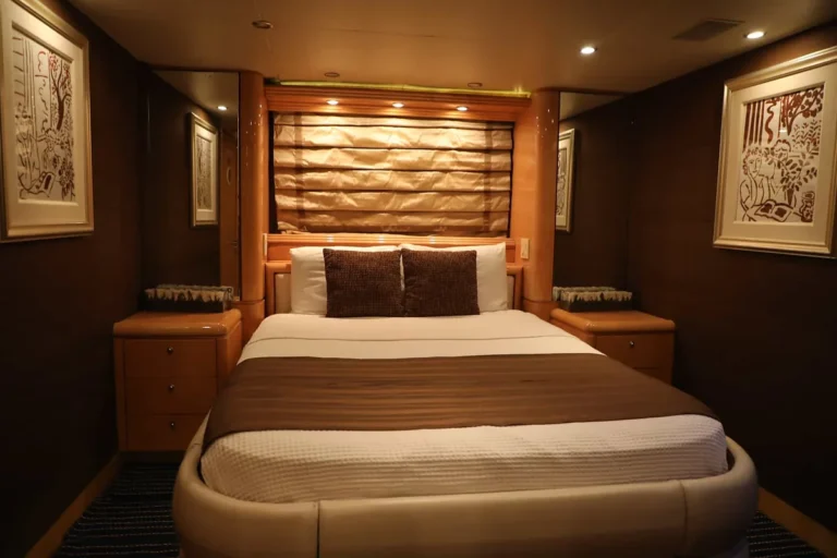 Guest stateroom aboard the 80′ Solstice yacht with a queen bed, warm wood paneling and framed art
